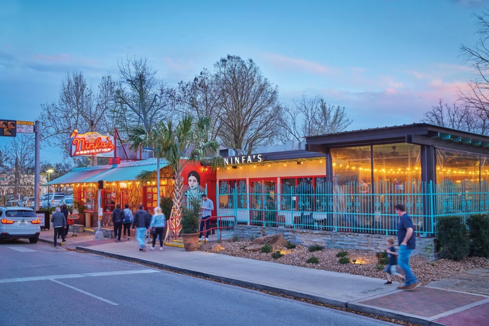 People walk past the colorful exterior of Ninfa’s restaurant at dusk, with bright lights and a mural.