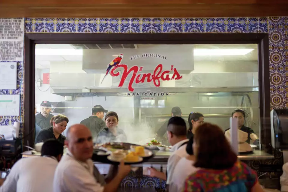 Cooks working in a busy kitchen behind a glass window at Ninfa's.