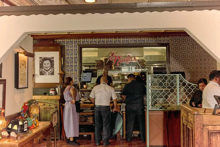 People are ordering food at a counter inside Ninfa's restaurant with colorful tiles and framed art on the walls.