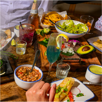 A table at Ninfa's set with sizzling fajitas, beans, rice, guacamole, and drinks, with people enjoying a meal.