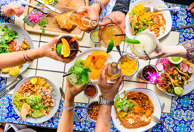 People raise drinks over a colorful table at Ninfa's filled with Mexican food and festive dishes.