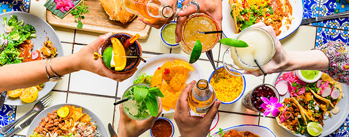 People raise colorful drinks over a table at Ninfa's filled with vibrant Mexican food and festive dishes.