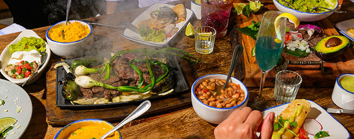 A table at Ninfa's set with sizzling fajitas, beans, rice, guacamole, and drinks, with people enjoying a meal.