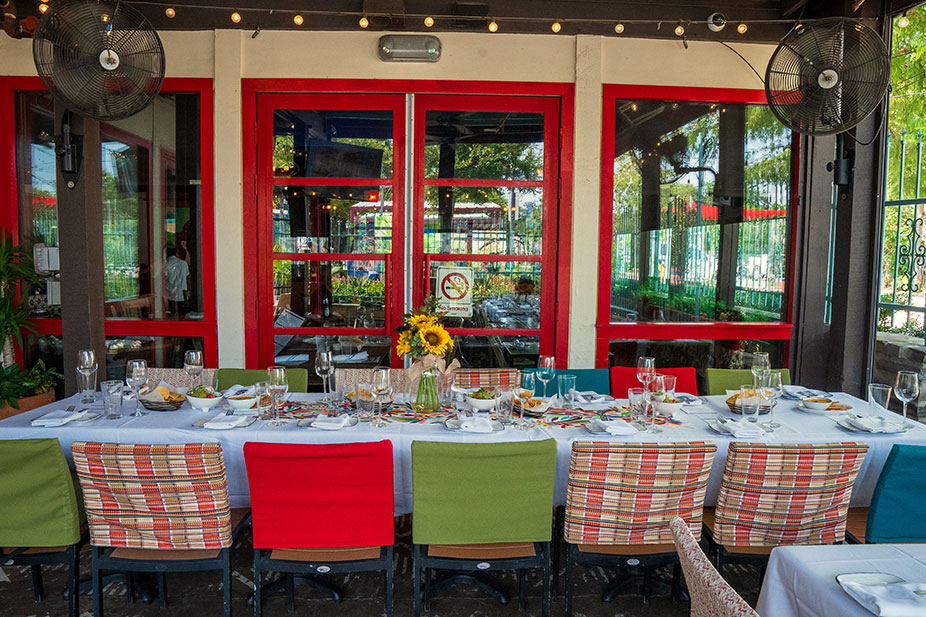 Outdoor dining table set for a meal, with colorful chairs and sunflowers, in the Front Patio at Ninfa's on Navigation.