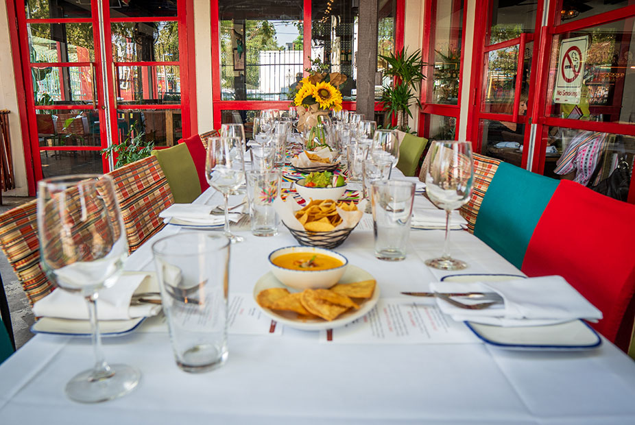 A long dining table set with glasses, plates, chips, and a sunflower centerpiece in the bright Front Patio at Ninfa's on Navigation.
