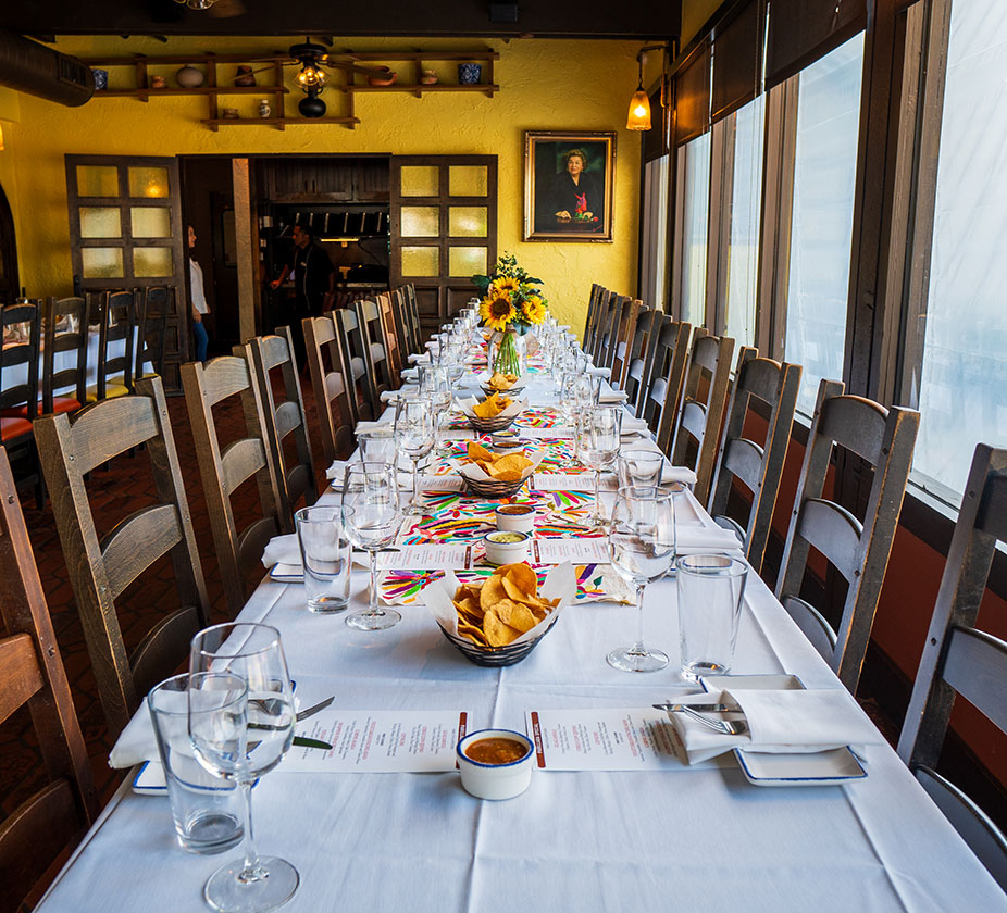 A long, elegant dining table set for a meal with menus, glasses, sunflowers, and chips in Mama's Room at Ninfa's on Navigation.