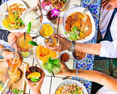 People raise drinks over a colorful table at Ninfa's filled with Mexican food and festive dishes.