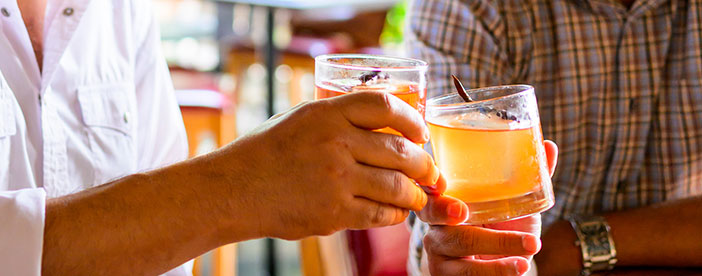 Two people at Ninfa's clinking cocktails garnished with cinnamon sticks.