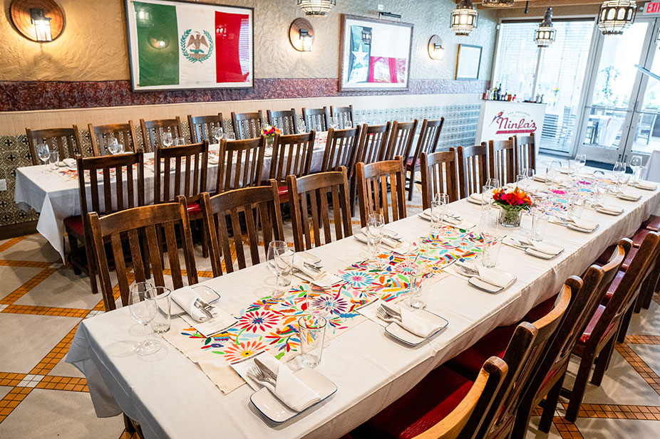 Elegant long tables set for dining, colorful table runners, and a Mexican flag on the wall of the Bandera Room at Ninfa's Uptown.