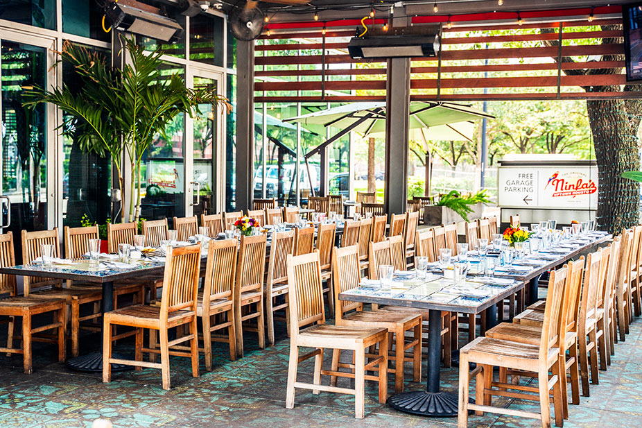 Enclosed Patio at Ninfa's Uptown with long wooden tables and chairs set for a large group, with plants and umbrellas.