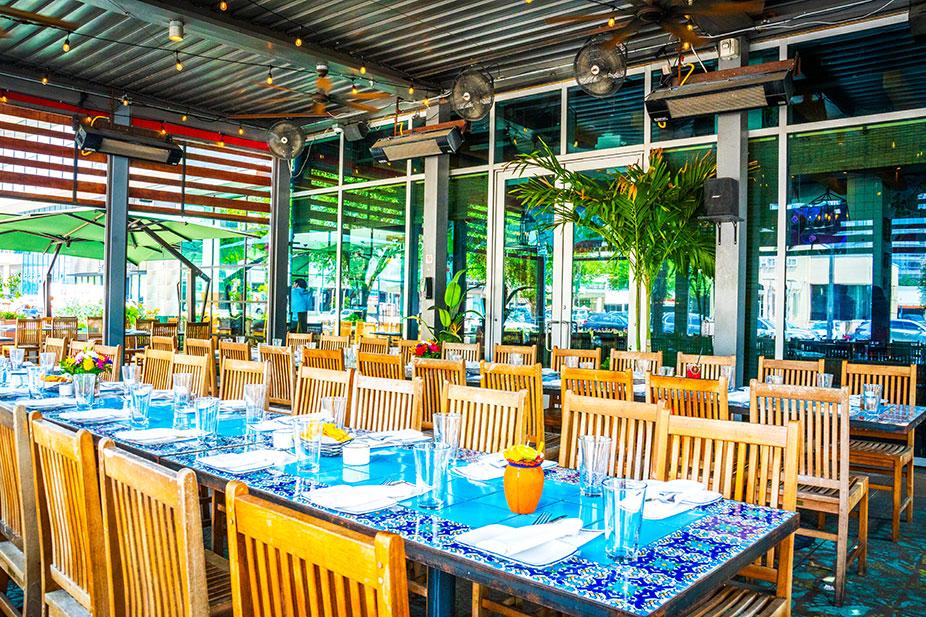 Enclosed Patio at Ninfa's Uptown with wooden chairs and tables set for dining, decorated with blue table runners.